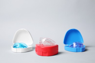 Photo of Transparent dental mouth guards in containers on light background. Bite correction