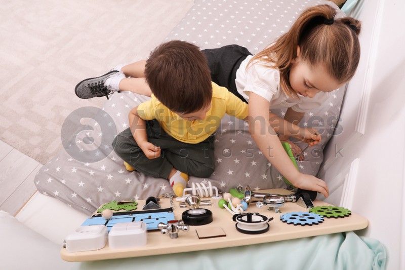 Little boy and girl playing with busy board on bed in room, above view