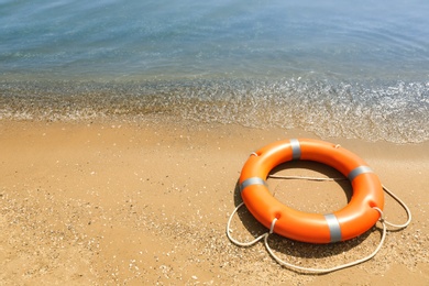 Orange life buoy on sand near sea. Emergency rescue equipment