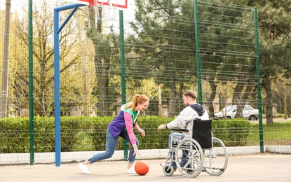 Man in wheelchair and young woman playing basketball on sports ground