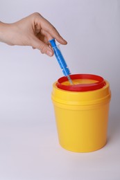 Woman throwing used syringe into sharps container on white background, closeup