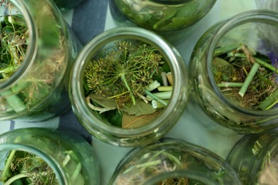 Glass jars with different herbs on table, flat lay. Pickling vegetables