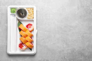 Food delivery. Delicious sushi rolls with soy sauce, ginger, wasabi, chopsticks in plastic container on light grey table, top view and space for text