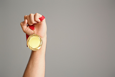 Man holding golden medal on grey background, closeup. Space for design