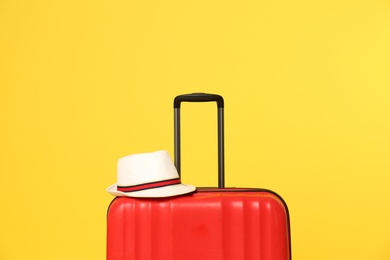 Bright suitcase with hat on color background