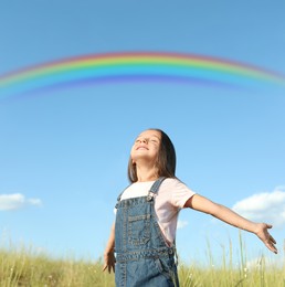 Beautiful rainbow in blue sky over cute little girl in field on sunny day