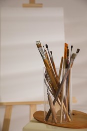 Holder with brushes and spatula near wooden easel in art studio