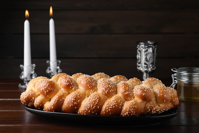 Homemade braided bread with sesame seeds, goblet and candles on wooden table. Traditional Shabbat challah