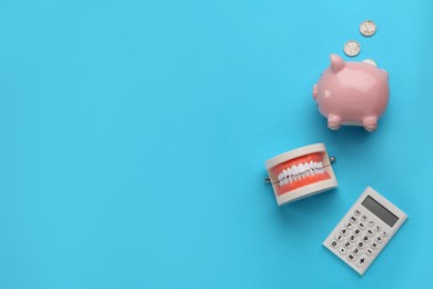 Educational dental typodont model, piggy bank and calculator on light blue background, flat lay with space for text. Expensive treatment