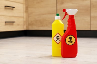 Photo of Bottles of toxic household chemicals with warning signs on floor indoors, space for text