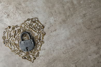 Heart made of keys, steel padlock and space for text on light stone background, top view. Safety concept