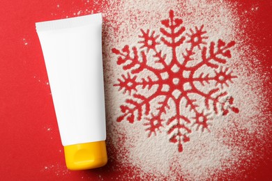 Photo of Winter skin care. Hand cream and snowflake silhouette made with artificial snow on red background, top view