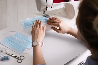Woman sewing disposable protective mask with machine at table, closeup