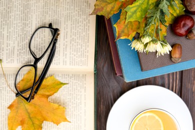 Maple leaves, books and cup of tea on wooden table, flat lay. Autumn atmosphere