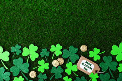 Flat lay composition with clover leaves and gold coins on green grass, space for text. St. Patrick's Day celebration