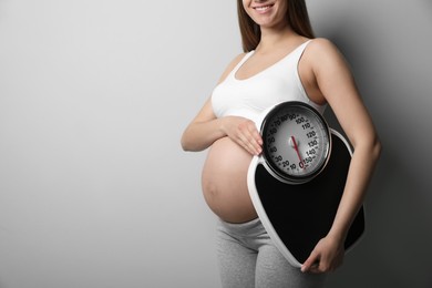 Pregnant woman with scales on grey background, closeup. Space for text