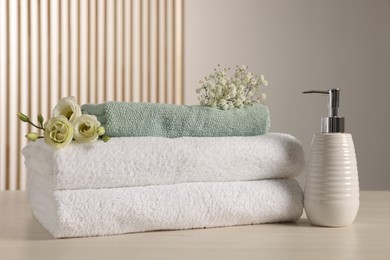 Soft folded towels, dispenser, gypsophila and eustoma flowers on light wooden table