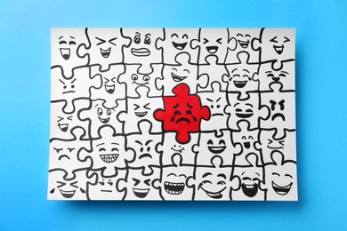 Drawing of white puzzle pieces and one red with different emotions on turquoise background, top view. Bullying concept
