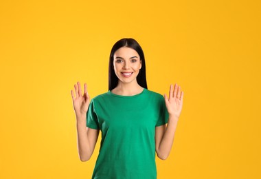 Attractive young woman showing hello gesture on yellow background
