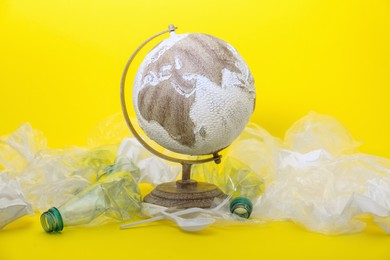 Photo of Globe in plastic bag and garbage on yellow background. Environmental conservation