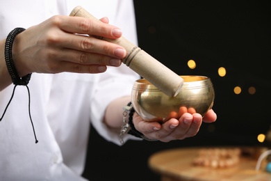 Woman using singing bowl in sound healing therapy on black background, closeup