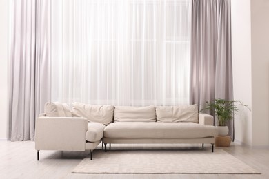 Photo of Comfortable sofa and window with beautiful curtains in room. Interior design