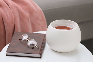 Wax air freshener, book and glasses on white table indoors. Interior element