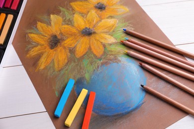 Colorful chalk pastels, pencils and beautiful painting of flowers on white wooden table, above view