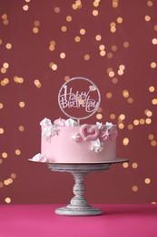 Beautifully decorated birthday cake on pink table against blurred festive lights