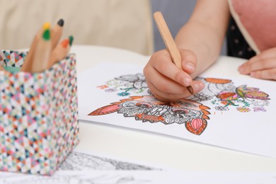 Little girl coloring antistress page at table, closeup