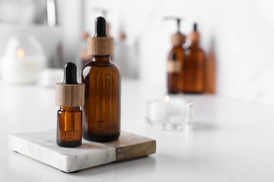 Bottles of essential oil on white countertop in bathroom, closeup. Space for text