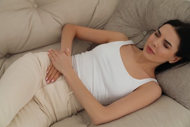 Woman suffering from appendicitis inflammation on sofa indoors