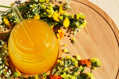 Delicious fresh honey in glass jar and beautiful flowers on wooden board. Space for text