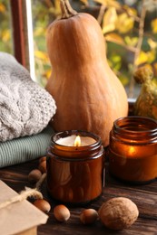 Photo of Burning scented candles, warm sweaters, acorns and pumpkins on wooden table near window. Autumn coziness