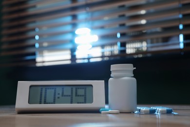 Digital alarm clock and pills on table indoors. Insomnia treatment