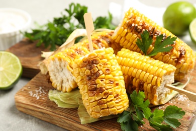Photo of Tasty grilled corn cobs with parsley on wooden board, closeup