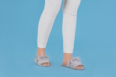 Photo of Woman in warm soft slippers on light blue background, closeup