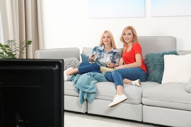 Photo of Young women with bowl of popcorn watching TV on sofa at home