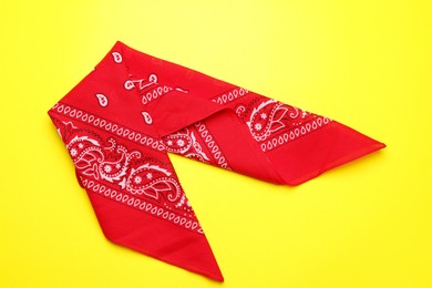 Folded red bandana with paisley pattern on yellow background, top view