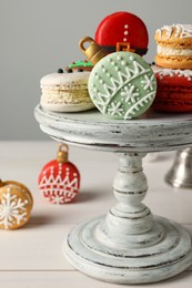 Photo of Stand with beautifully decorated Christmas macarons on white wooden table