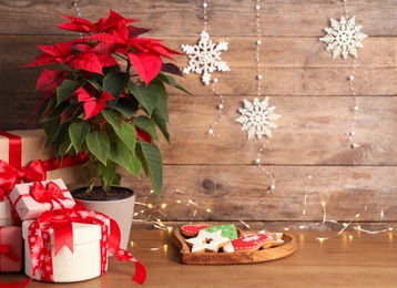 Poinsettia (traditional Christmas flower), gift boxes and cookies on wooden table