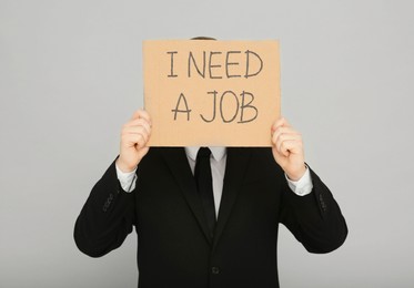 Photo of Unemployed man holding sign with phrase I Need A Job on light grey background