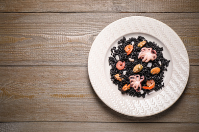 Photo of Delicious black risotto with seafood on wooden table, top view. Space for text