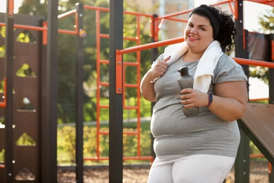 Beautiful overweight woman with towel and bottle on sports ground