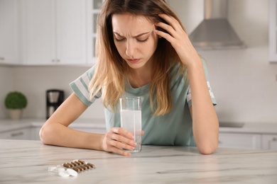 Woman holding glass of medicine for hangover in kitchen