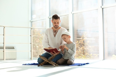 Muslim man and his son reading Koran together indoors