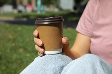 Woman holding takeaway cardboard coffee cup with plastic lid in park, closeup