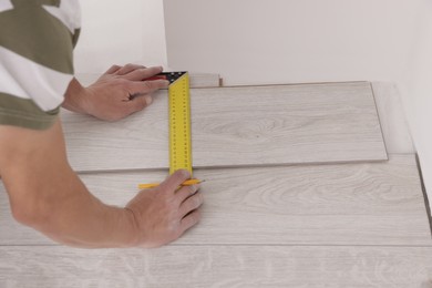 Photo of Professional worker using measuring tape during installation of laminate flooring indoors, closeup