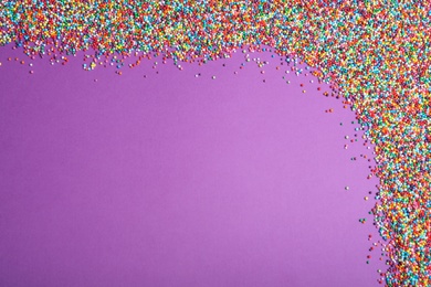 Colorful sprinkles on purple background, flat lay with space for text. Confectionery decor