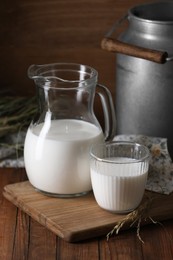 Photo of Tasty fresh milk in can, jug and glass on wooden table